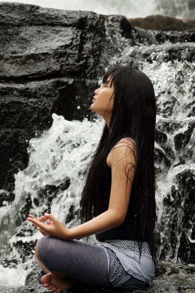 Woman meditating peacefully beside flowing waterfall representing mindful emotional balance and inner calm